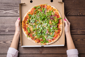 Woman holding pizza in cardboard box. Top view