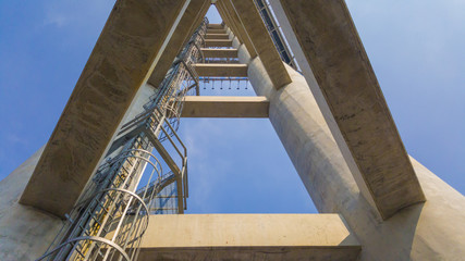 Abstract cement structures with ladder to the top on blue sky background.