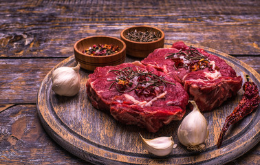 Raw Beef Steak, salt, pepper, garlic, rosemary  on the wooden board, background.