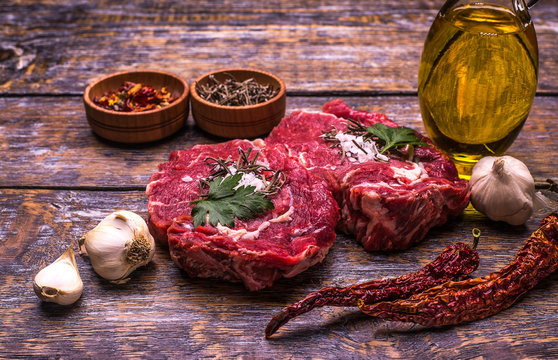Raw Beef Steak, salt, pepper, garlic, rosemary  on the wooden board, background.