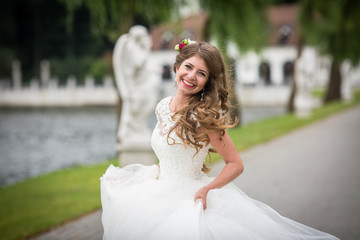 Cheerful bride with long dark blonde hair whirls on path in park
