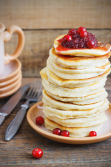Stack of delicious pancakes with cranberries on plate and napkin wooden background