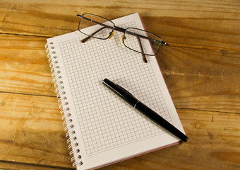 Notebook with glasses and fountain pen on wooden desk