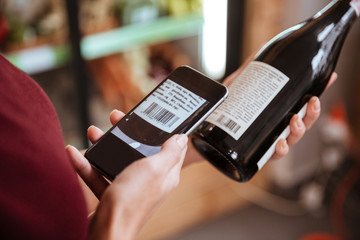 Woman scanning bar code with mobile phone on wine bottle