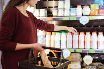 Woman with basket choosing and buying yoghurt in supermarket