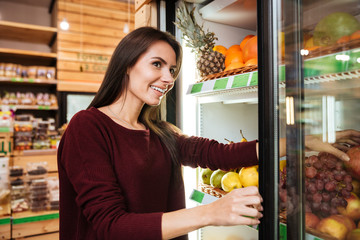 Smiling woman choosing and buying fruits at grocery shop