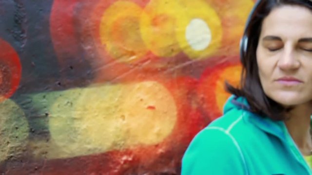 woman listen music against graffiti wall, steadycam shot, slow motion shot
