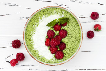 Matcha green tea chia seed pudding bowl, vegan dessert with raspberry and coconut milk. Overhead, top view, flat lay
