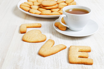 LOVE-shaped cookies and a white cup of tea on white wooden table. Cookies for Valentines Day.