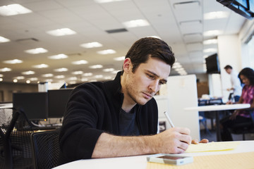 A man sitting at a table in an office writing.