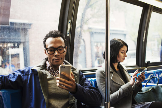 A young man and a young woman sitting on public transport looking at their cellphones.