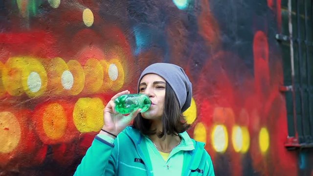 Hipster woman drinking water from a bottle, steadycam shot, slow motion shot
