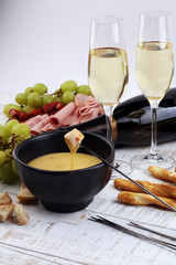Gourmet Swiss fondue dinner on a winter evening with assorted cheeses on a board alongside a heated pot of cheese fondue with two forks dipping bread and white wine behind in a tavern or restaurant