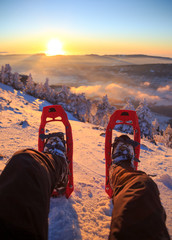 Winter sport activity. Male hiker looking over his snowshoes at the beautiful landscape in the French Vercors mountains during sunset.