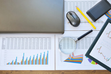 Financial printed paper charts, graphs, diagrams, computer and phone on  wooden desk