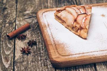 A piece of sliced apple pie with cinnamon on vintage wooden background texture.