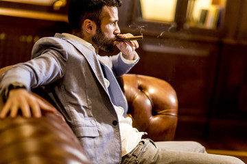 Handsome man sitting on a leather sofa and smoking cigar