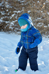Fototapeta na wymiar young toddler boy dressed in warm jacket scarf and hat playing in winter snow