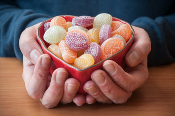 détail main d'homme tenant un bol en forme de coeur contenant des bonbons