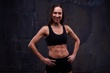 Smiling muscular trainer woman posing against black background