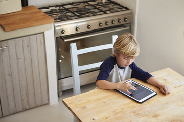 Fototapeta na wymiar Young boy using tablet computer in kitchen, elevated view