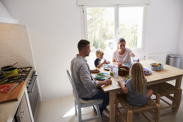 Family sitting down to eat lunch at kitchen table