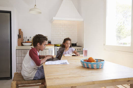 Brother and sister doing homework at kitchen table - Powered by Adobe