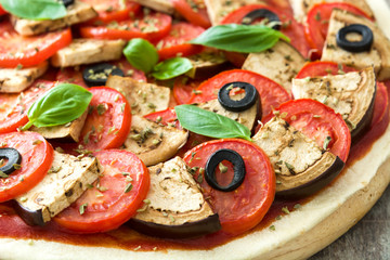 Vegetarian pizza with eggplant, tomato, black olives, oregano and basil on wooden background