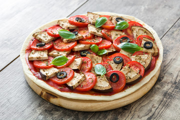 Vegetarian pizza with eggplant, tomato, black olives, oregano and basil on wooden background