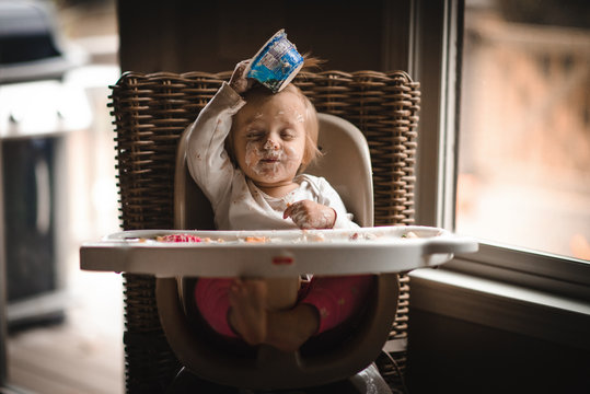 Messy girl sitting in highchair covered in food