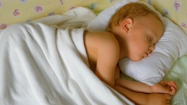 Close-up portrait of a sleeping baby in white bed