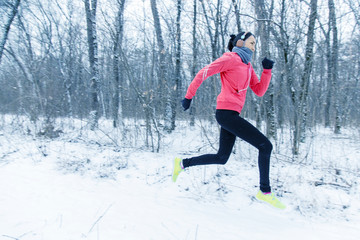 Running sport woman. Female runner jogging in cold winter forest wearing warm sporty running clothing and gloves headphones. Beautiful fit  female fitness model.