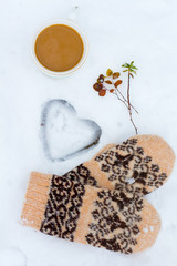 composition in the snow from a cup of coffee, knitted gloves and twigs with herbs