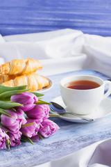 Breakfast with croissants tea purple tulips on blue wooden tray.