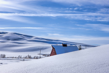 The roof of a red barn peaks over a snowy hill in this winter vista in Moscow, Idaho.