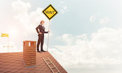 Young businessman on house brick roof holding yellow signboard. 