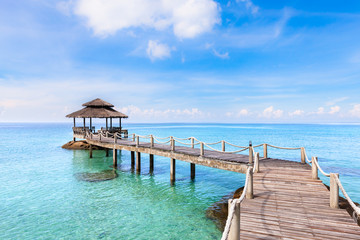 Tropical beach landscape with wooden pier above transparent sea