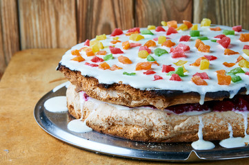 Rustic homemade birthday cake. Simple and delicious cake for the holiday with white cream and colored decor. Sponge, sour cream, cherry filling and colored candied fruits. Domestic recipe.