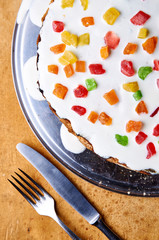 Cute cake with white cream and multi-colored candied fruits, dried fruits. Served tables in the room for the holiday with bright cake. Treats for birthday or Valentine's Day. Top view of the dessert.