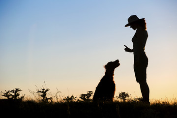 Silhouette of a female as training her dog. Pet training concept.