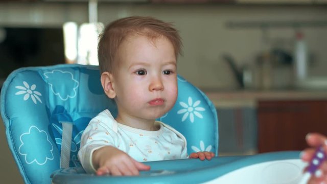 Mom is feeding little infant boy broccoli puree with spoon. He smiles and shows somewhere by his hand. Dont' like broccoli