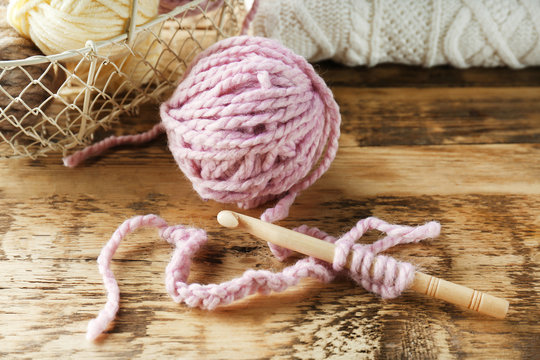 Pink ball of knitting yarn and hook on wooden table