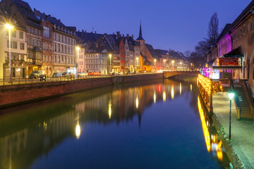 Picturesque quay and church of Saint Nicolas with mirror reflections in the river Ile and Christmas garland during morning blue hour, Strasbourg, Alsace, France