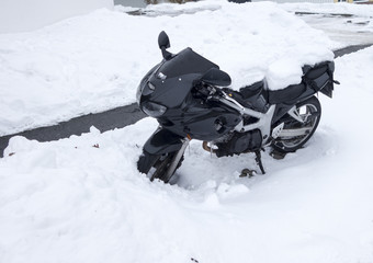 Snow covered motorcycle at the roadside of a snowy road