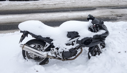 Snow covered motorcycle at the roadside of a snowy road