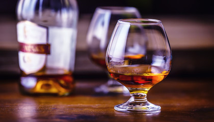 Glass whiskey cognac brandy or rum.One half full glasses of cognac on a wooden surface.