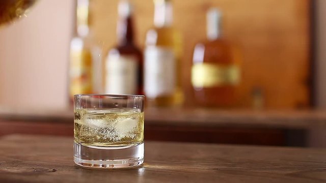 Pour whiskey into a glass placed on a wooden table