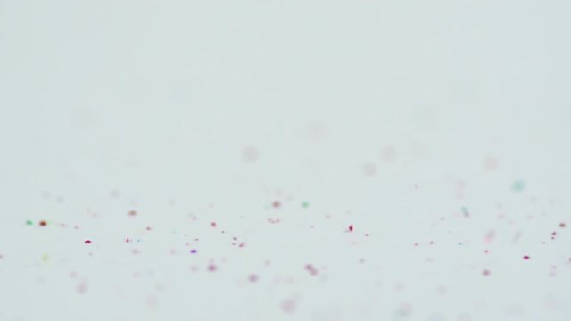 Shiny glitter particles falling and hitting a clean white surface. Red, blue, gold and green glitter mixed together