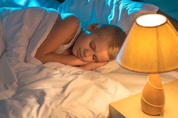 The boy sleeping on the bed near the bedside lamp