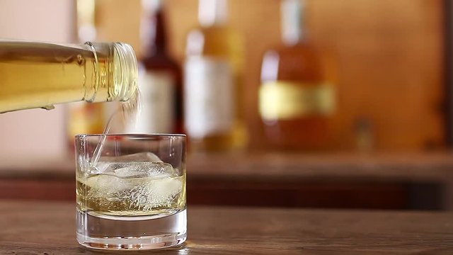 Pour whiskey into a glass placed on a wooden table. Slow motion